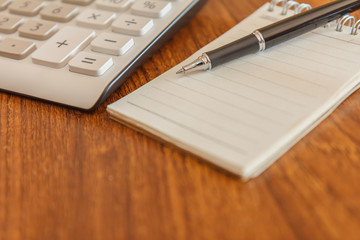 Blank notebook with pen and calculator on wooden table, business concept