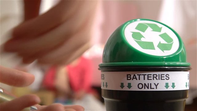 Female hands putting used batteries into special recycling box at home. Child playing on the background. Separating Domestic waste. Batteries Only. Slow motion