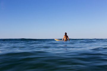 A female surfer on a calm ocean patiently waits for a wave.