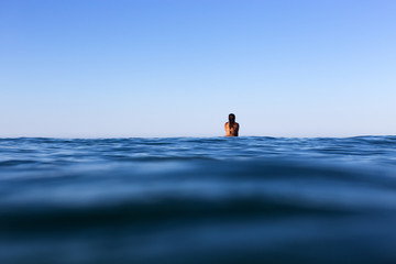 A surfer sits on her board waiting for a wave on a glassy calm ocean in Australia.