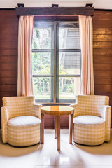 Classic twin fabric sofas and wooden round table. Interior design with window and curtains.