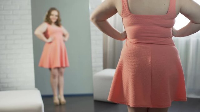Confident overweight woman admiring reflection of her plus size body in mirror