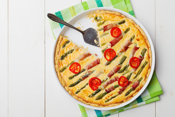 Tart with asparagus and tomatoes on white wooden background.