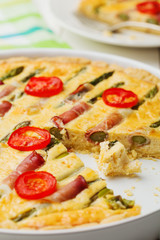 Tart with asparagus and tomatoes on white wooden background.