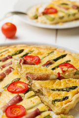 Tart with asparagus and tomatoes on white wooden background.