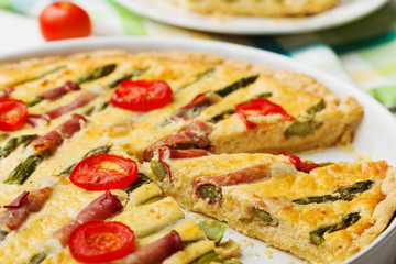Tart with asparagus and tomatoes on white wooden background.