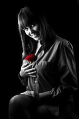 Portrait of young and attractive woman close up on black background with rose in her hand. Looking forward at something or somebody. Beautiful smile.