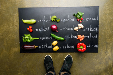partial view of man standing near fresh vegetables and calories table, healthy lifestyle concept - obrazy, fototapety, plakaty