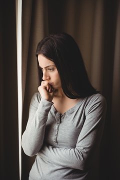 Thoughtful woman standing against curtain