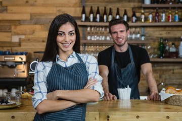 Portrait of smiling waitress and waiter standing at counter - obrazy, fototapety, plakaty