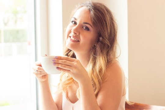 A beautiful young woman sitting in a cafe. Girl drinks Cappuccino.