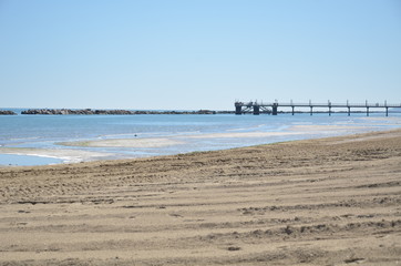 wooden pier on the beach with a girl walking 