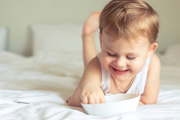 Fototapeta na wymiar Little cute boy having breakfast in bed. Boy playing in bed. Breakfast in bed.