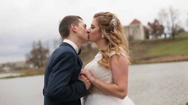 Happy young bride and groom kissing each other near the lake. Wedding couple