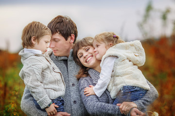 A big family for a walk in the country park. Mom smiles and holds her daughter in her arms. Father gently hugs a serious son.