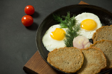 Homemade food. Tasty breakfast. Appetizing fried egg with potato pancakes and herbs in dripping pan  on a black background