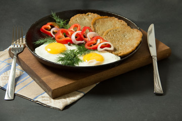 Homemade food. Tasty breakfast. Appetizing fried egg with potato pancakes and herbs in dripping pan  on a black background