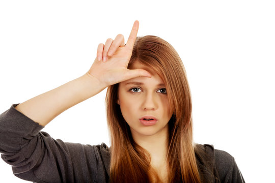Teenage woman makes loser sign on her forehead