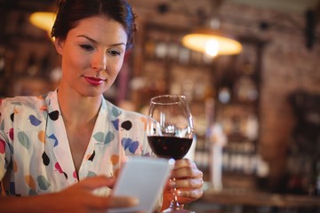 Young woman using mobile phone while having wine