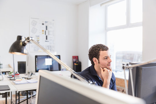 Mid adult man in office using computer hand on chin