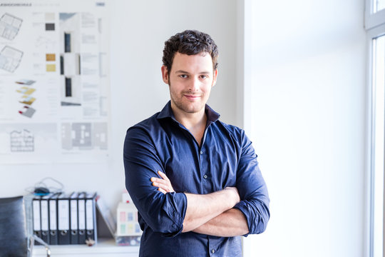 Mid adult man in office arms folded looking at camera smiling