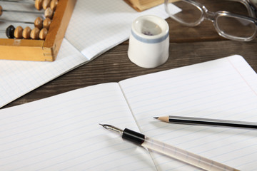 A penholder  with a pen, a pencil, an inkwell, glasses and abacus. lie on an old wooden table. View from above