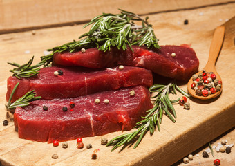 Raw beef steak on a cutting board with rosemary and spices.
