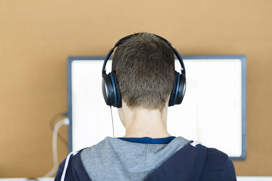 A Young Man Behind A Computer Screen With Headphones On, Seen From The Back.