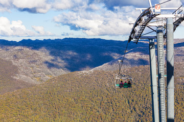 People sitting on Kosciuszko Express Chairlift in front of beautiful view.