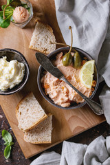 Black bowl of salmon pate with red caviar served with butter, sliced bread, capers, vintage knife,...