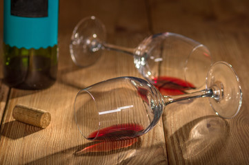 Empty bottle of red wine, two lying wine glasses and wine cork on wooden background 
