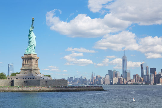 Statue of Liberty and New York city skyline in a sunny day, blue sky and approaching white clouds