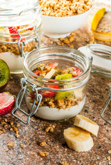 Healthy breakfast. Diet. Overnight oatmeal in a can, muesli. Yogurt with homemade granola and organic fruits - kiwi, banana, strawberry. On the stone table. With ingredients and spoons. 