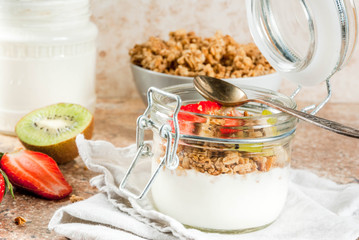Healthy breakfast. Diet. Overnight oatmeal in a can, muesli. Yogurt with homemade granola and organic fruits - kiwi, banana, strawberry. On the stone table. With ingredients and spoons. 