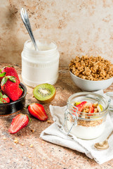 Healthy breakfast. Diet. Overnight oatmeal in a can, muesli. Yogurt with homemade granola and organic fruits - kiwi, banana, strawberry. On the stone table. With ingredients and spoons. 
