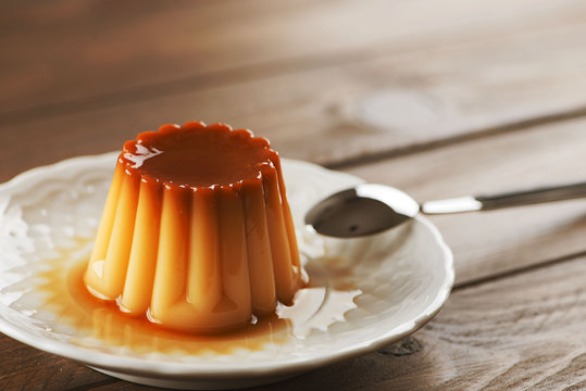 From above white plate with flan and spoon on the wooden background. Horizontal shoot.