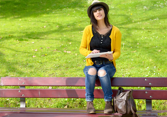 young brunette girlsitting on a bench with a tablet in park