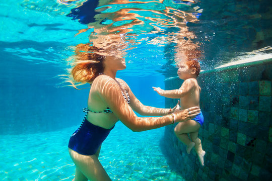 Happy family - mother, baby daughter learn to swim. Girl dive in swimming pool with fun - jump underwater with splashes. Lifestyle, summer children water sports activity, swimming lessons with parent.