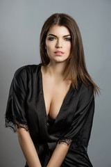 Fototapeta premium young girl in black lingerie and black satin robe on a light background