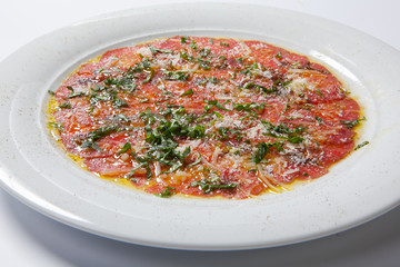 Beef carpaccio served with ruccola on a white plate