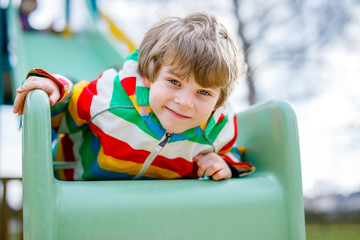 Fototapeta na wymiar Happy blond kid boy having fun and sliding on outdoor playground