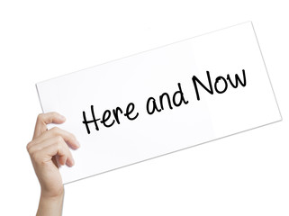 Here and Now Sign on white paper. Man Hand Holding Paper with text. Isolated on white background
