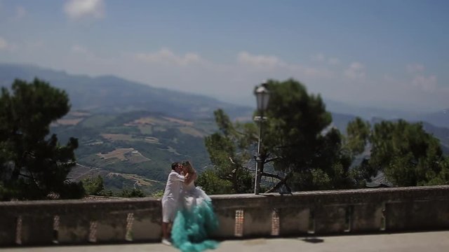 Groom and bride in dress with turqoise skirt kiss before beautiful landscape