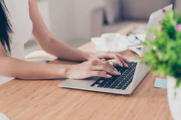 Close up cropped photo of nice hands of woman typing on the laptop at the top of wooden table