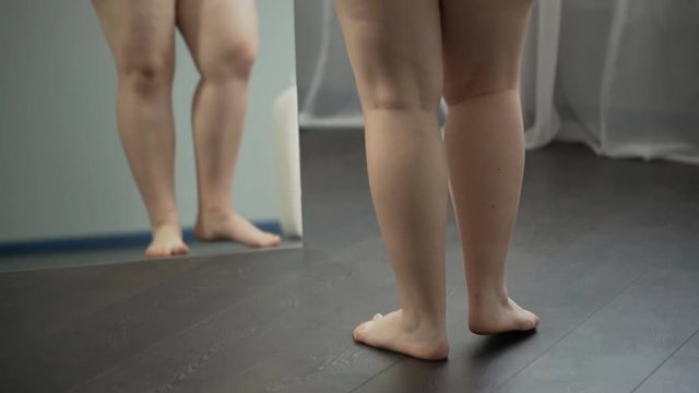 Girl examining in mirror her sagging cellulite body, pondering about surgery