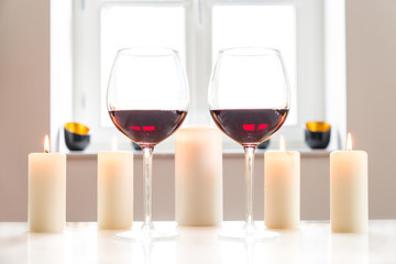 Zwei Gläser mit Rotwein auf einem weißen Tisch vor weißem Hintergrund und Fenster