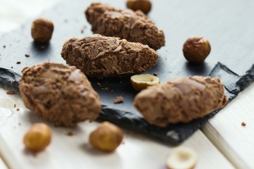 Chocolate truffle pralines covered with milk chocolate shavings and decorated by hazelnut kernels on slate stone serving board and on white wood table