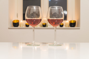 Zwei Gläser mit Rotwein auf einem weißen Tisch vor weißem Hintergrund und Fenster
