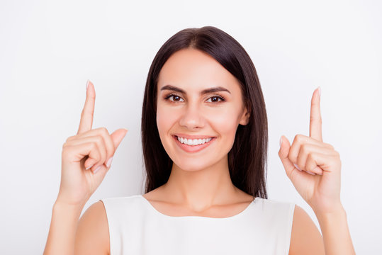 Close up portrait of young cheerful pretty girl gesturing up with her fingers. She is smiling, standing on the white background