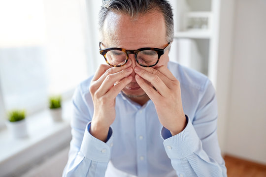 businessman in glasses rubbing eyes at office